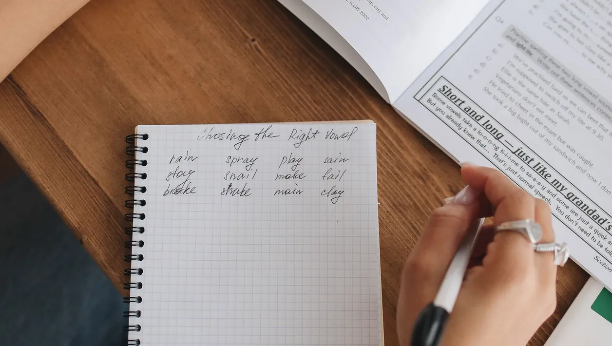 Person writing a list of tasks next to a laptop