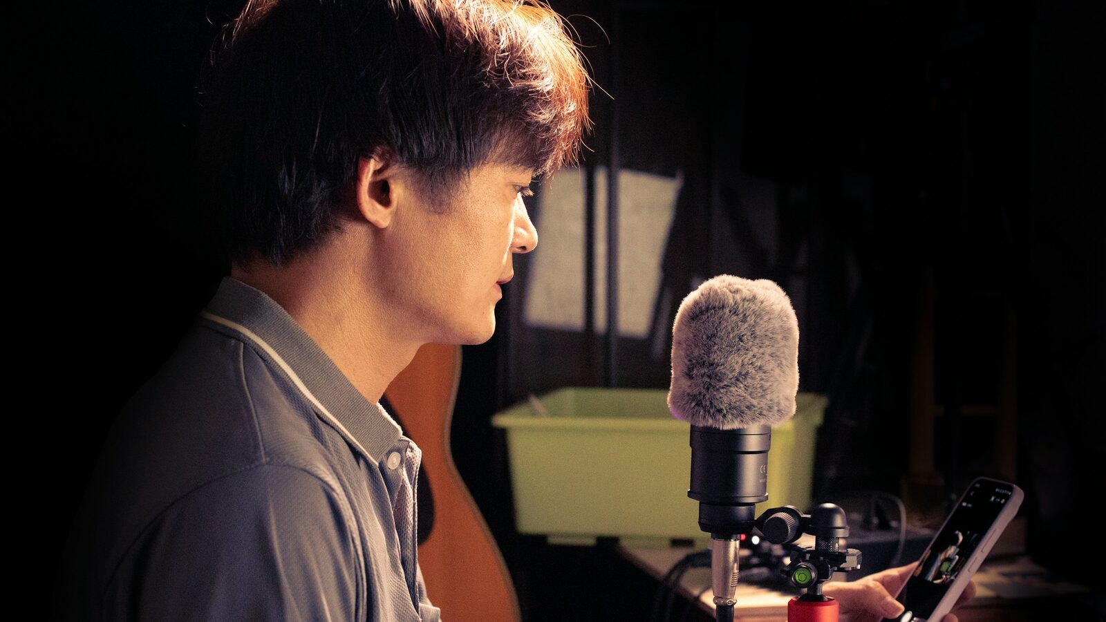 Man recording his voice into a microphone with a smartphone in hand