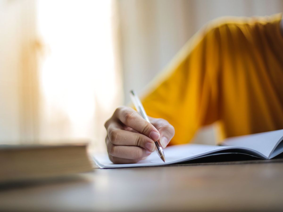 Person writing notes next to a laptop
