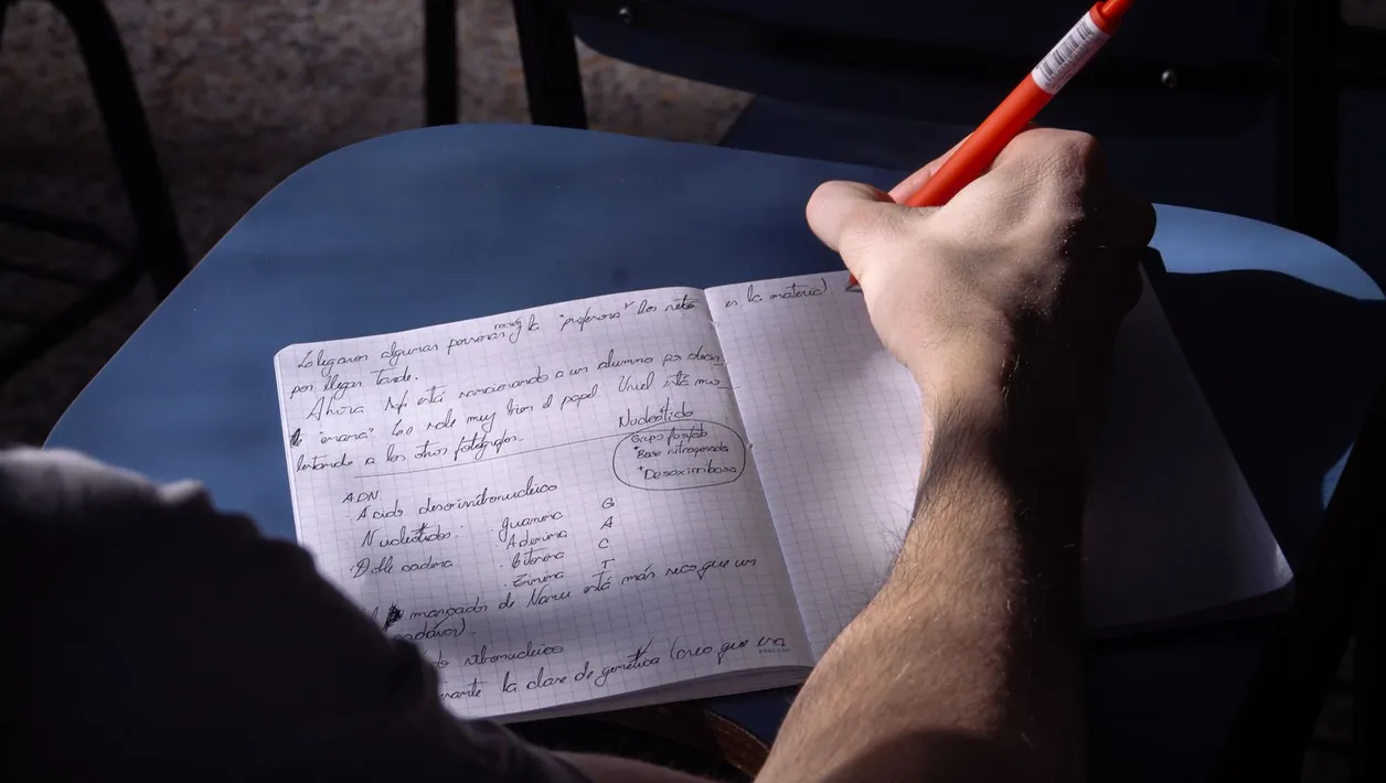 Person writing a test plan in a notebook next to a laptop
